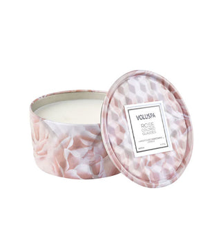 Light pink rose-patterned Rose Colored Glasses scented Voluspa candle tin with faceted texture has its lid removed and propped up alongside