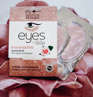 Outer pack of ToGoSpa Eyes Rose Gold Sparkle Bomb eye masks with inner foil pack emerging from it rest on pink flower petals