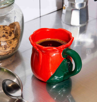 Red and green ceramic rose mug holds black coffee on a stainless steel countertop staged with kitchen items