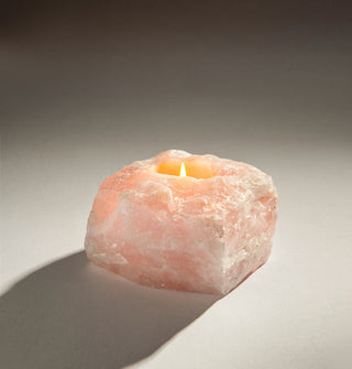 A small flame glows from within a squarish pink rose quartz crystal formed into a candle holder
