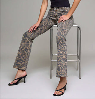 Model seated on a steel stool wears a pair of flared tiger stripe jeans paired with strappy black heels