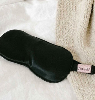 Black satin Kitsch eye mask on a soft white surface with knit blanket