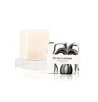 Two 2-ounce bars of Sea Salt & Lavender Shea Butter Soap, one wrapped in black and white octopus print paper and the other unwrapped on a clear rectangular pedestal