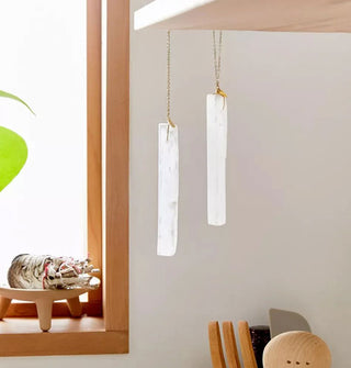 Two elongated pieces of selenite hang from gold chain that has been attached to a kitchen shelf edge