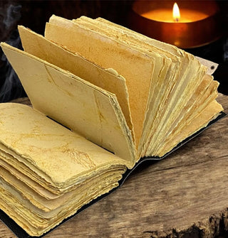 Opened notebook with rough, deckle edge pages on a rustic wooden platform in front of a lit candle in amber glass