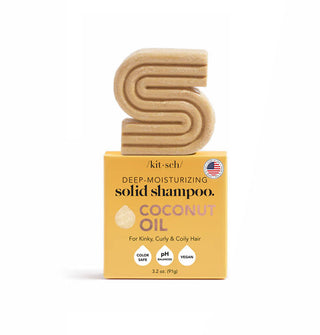 Gold S-shaped ribbed Kitsch Deep-Moisturizing Coconut Oil Solid Shampoo bar rests on top of its orange box packaging