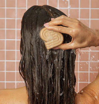 Model applies a lightly lathered bar of shampoo to wet hair against a tiled backdrop
