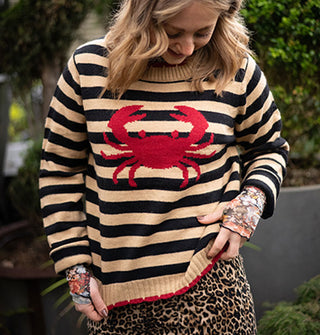 Model wears a beige and black striped sweater with red crab design on the front