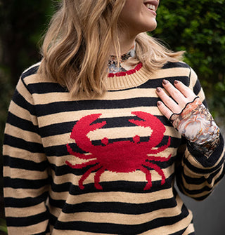 Smiling model wears a beige and black striped sweater with red crab design on the front