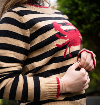 Model wears a beige and black striped sweater with red trim and red crab design on the front