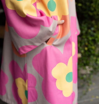 Model poses with hand in the pocket of an overcoat with large floral print in a gray, pink, orange, yellow and green color palette