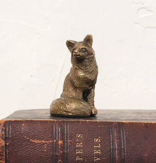Brass sitting fox figurine on top of an antique leather-bound book