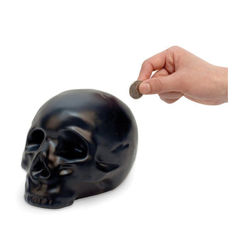 Model's hand holds a coin near the top of a black skull-shaped money bank