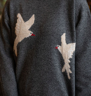 Closeup of two white birds with black eyes and red beaks on a dark heather gray sweater