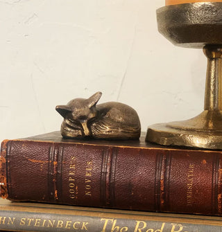 Brass sleeping fox figurine rests on a leather bound book next to a gold-toned pedestal candle holder