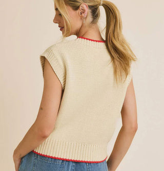 Model wears a sleeveless cream-colored sweater with red-rimmed neckline and bottom hem