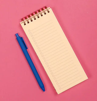 Long rectangular spiral-bound notepad with printed checklist and a blue pen alongside rest on a pink surface