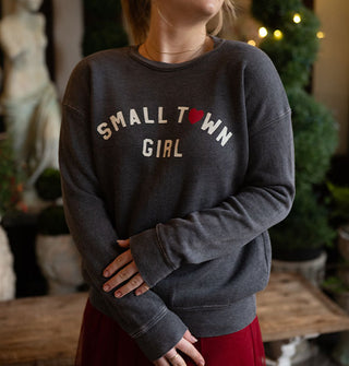 Model wears a dark gray sweatshirt that says, "Small town girl" in white lettering with a red heart in place of the "O" in "Town"