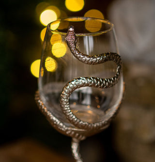 Wine glass with a clear bowl and silver snake wrapped partially around it in front of twinkling background lights
