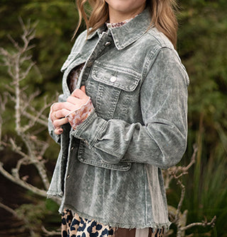 Model wears a stone wash-effect blue-gray corduroy peplum jacket against a grassy backdrop