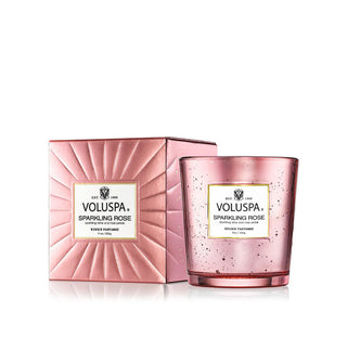 Speckled pink glass Voluspa Sparkling Rose candle jar sits next to its metallic pink gift box with decorative grooves