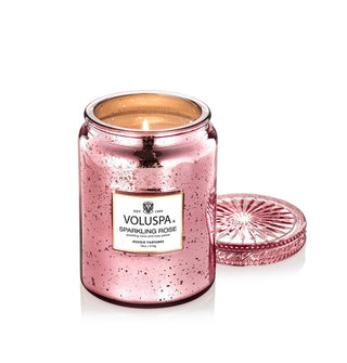 Speckled pink glass Voluspa Sparkling Rose candle jar with flame inside and matching lid removed and set behind and to the side