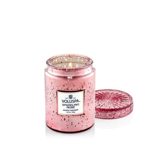 Speckled pink glass Voluspa Sparkling Rose candle jar with matching embossed lid that has been removed and set to the side to reveal a lit wick inside the jar