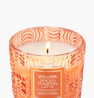 Lit single-wick Spiced Pumpkin Latte Voluspa candle in an orange embossed glass vessel