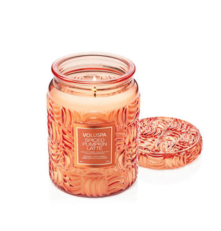 Lit single-wick Spiced Pumpkin Latte Voluspa candle in an orange embossed glass jar with matching lid set to the side