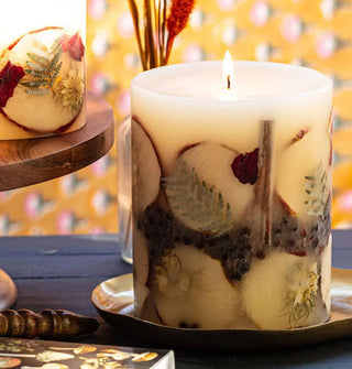 Lit single-wick pillar candle with embedded apple slices, ferns, cinnamon sticks