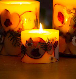 Lit pillar candles in a darkened space, each with apple slices, ferns, and flowers embedded in their wax
