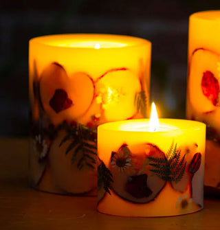 Lit pillar candles in a darkened scene, each embedded with apple slices, ferns, flowers, and other botanicals