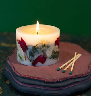Lit single-wick stout pillar candle alongside three wooden matchsticks with apple slices, flowers, and ferns embedded in its wax