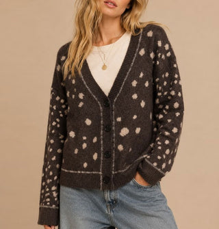 Model with one hand in pocket wears a brown V-neck cardigan with light spots all over and a thin light line along the neckline, button placket, and sleeve cuffs