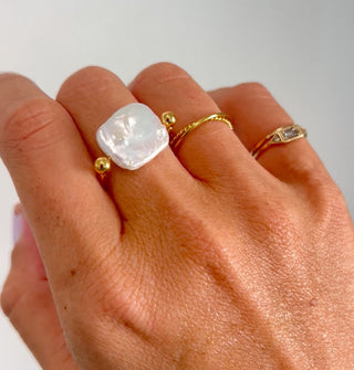 Model wears a gold and pearl ring with other thin gold ring bands