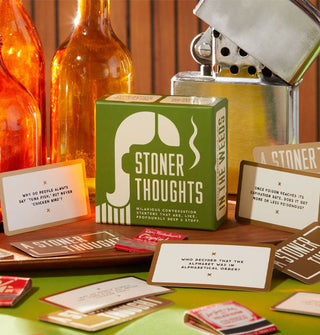 Stoner Thoughts game box and cards are staged with orange glass bottles and a gigantic silver lighter prop