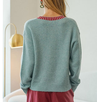 Model with back turned to camera wears a powder blue cardigan with red striped neckline