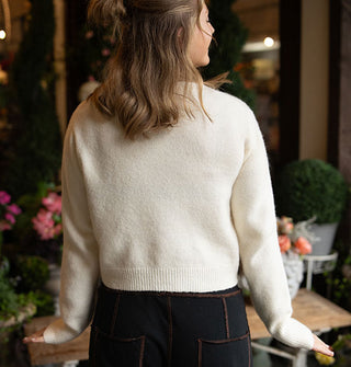 Model facing away from the camera wears a white long-sleeved sweater