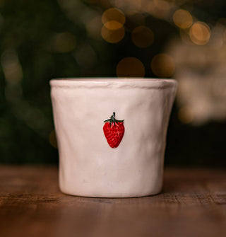 Rustic cream-colored ceramic pot with bright red strawberry accent on a wooden tabletop