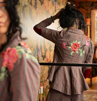 Model's reflection in mirror shows embroidered floral appliqués on the back of a red-striped gray tailored blazer
