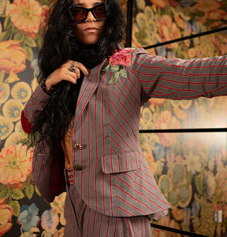 Model in sunglasses holds out one arm of a tailored gray and red striped blazer with mismatched buttons and embroidered floral shoulder appliqué