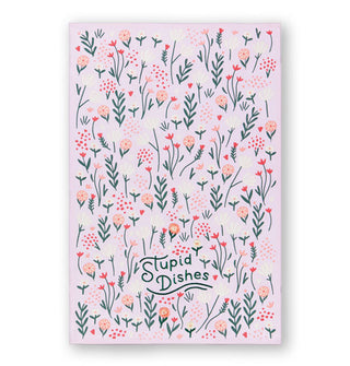 Rectangular white cloth featuring all-over whimsical floral designs says, "Stupid Dishes" in dark green embroidery near the bottom