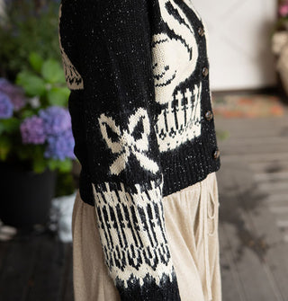 SIde view of a black button-down cardigan with white swan, bow, and other designs