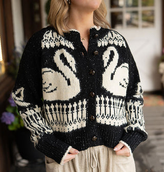 Model wears a black button-down cardigan with swans, bows, and intricate border designs, and white edging along the neckline and sleeve cuffs