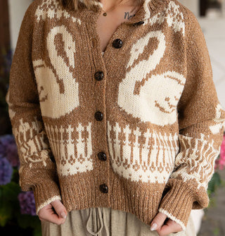 Model wears a brown button-down cardigan with swans, bows, and intricate border designs, and white edging along the neckline and sleeve cuffs