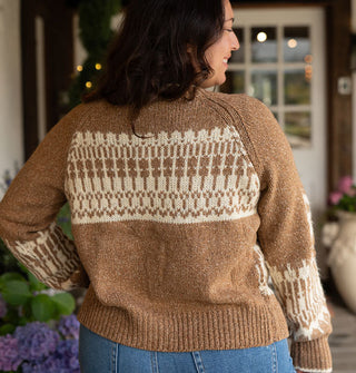Model with back to camera wears a brown sweater with an intricate white intarsia design on the back and around the lower sleeves
