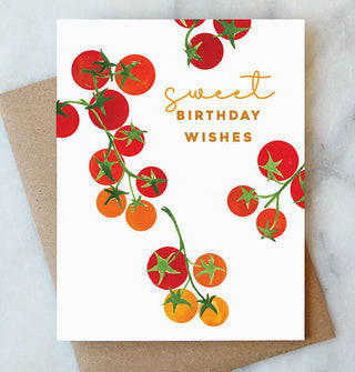 White greeting card featuring watercolor artwork of cherry tomatoes on the vine says, "Sweet birthday wishes" in gold foil lettering; a kraft paper envelope rests underneath