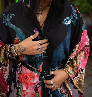 Model wears a black belted robe with ultra-wide sleeves and an all-over print of large, colorful flowers and peacocks