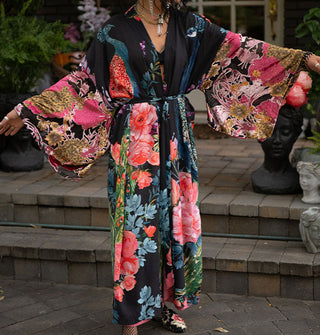 Model with arms outstretched wears an ankle-length black robe with ultra-wide sleeves and an all-over print of large, colorful flowers and peacocks