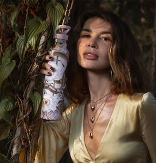 Model holds a slender snake and flowers water bottle against a botanical backdrop